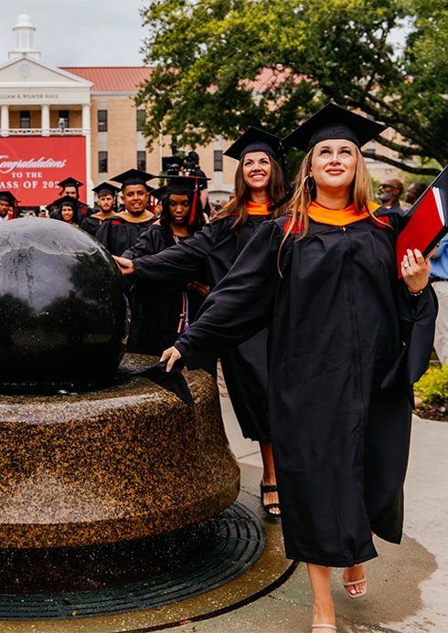 graduates touching globe statue